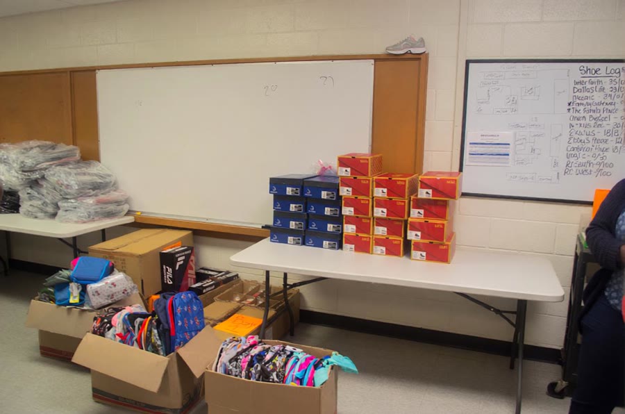A classroom table and floor stacked with boxes and bags of donated supplies.